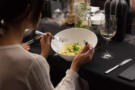 Woman eating in a restaurant fresh summer salad with vegetables cabbage, spinach, parsley, greens in white bowl. Vegetarian healthy food.の写真素材