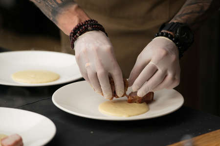 Closeup of chief in white gloves serving delicious roasted pork meat wrapped in bacon with puree. Irish traditional dish wrapped pork loin with roasted garlic.の写真素材