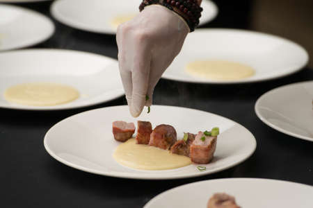 Closeup of chief in white gloves serving delicious roasted pork meat wrapped in bacon with puree. Irish traditional dish wrapped pork loin with roasted garlic.の写真素材