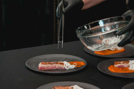 chef in a black gloves in a restaurant finishing a dish from tuna steak on a wooden plank