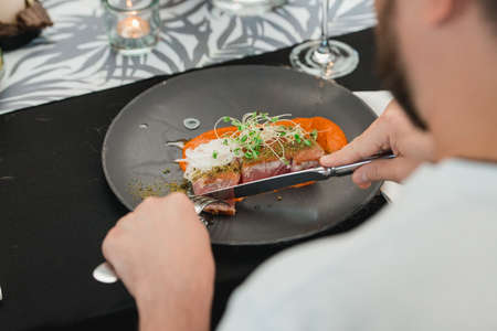 man eating grilled tuna steak with onion on a gray ceramic plate. Selective focus, close-up.の写真素材