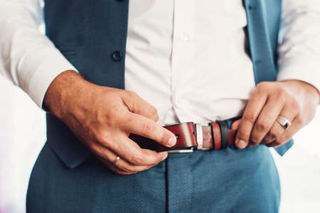 Businessman putting on a belt, fashion and clothing concept, groom getting ready in the morning before ceremony. Blue suitの写真素材