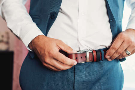 Businessman putting on a belt, fashion and clothing concept, groom getting ready in the morning...