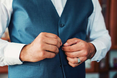 The man fastens the cuffs of the waistcoat. Morning of the groom. Hands of wedding groom buttoning...