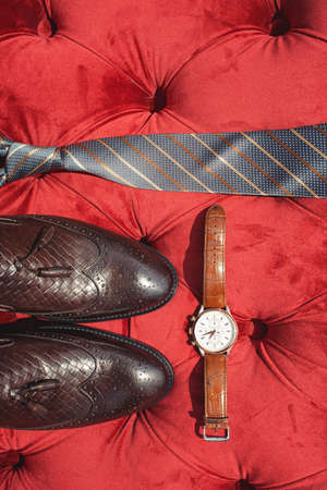 Businessman accessories. Men's Accessories: Men's tie, brown shoes and watch. Grooms Set on red sofaの写真素材