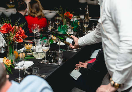 Waiter pouring red wine in a glass at a served restaurant tableの写真素材