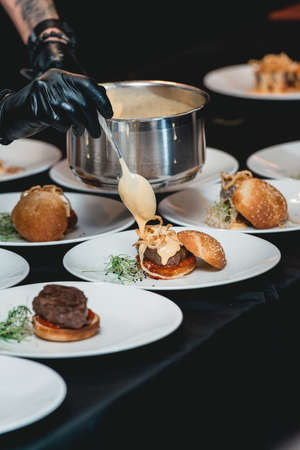 chef in a black gloves serving a burgers on the table in a restaurant. Black tableclothの写真素材