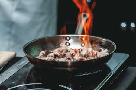 The chef cooks small octopus on a metal frying pan at the restaurant to make brazilian dish. Pan is on fire.の写真素材