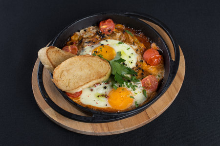 healthy breakfast shakshuka - fried eggs, onion, bell pepper, tomatoes and spices in cast iron stewpan on old wooden plank.の写真素材