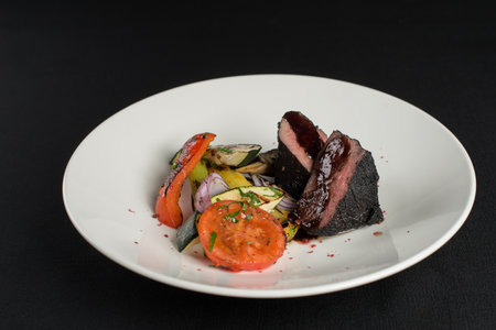 veal tenderloin in ashes with grilled vegetables on a white plateの写真素材