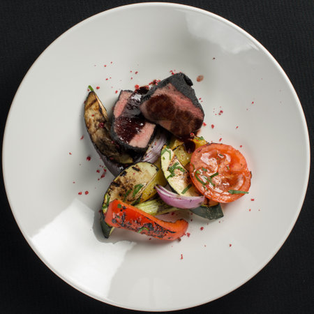 veal tenderloin in ashes with grilled vegetables on a white plateの写真素材