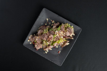 Salad with smoked duck meat, sweet and sour sauce with almonds flakes on a black ceramic plateの写真素材