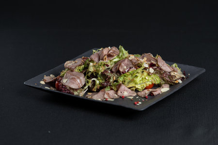 Salad with smoked duck meat, sweet and sour sauce with almonds flakes on a black ceramic plateの写真素材