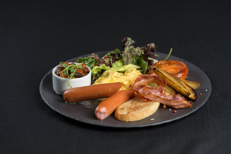 Traditional English breakfast on a white plate. Sausage, beans, eggs, bread and salad. Black tableclothの写真素材