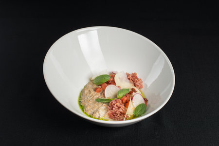 Bowl with delicious salted oatmeal, bacon and vegetables on a black tableclothの写真素材