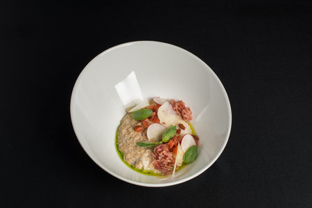 Bowl with delicious salted oatmeal, bacon and vegetables on a black tableclothの写真素材