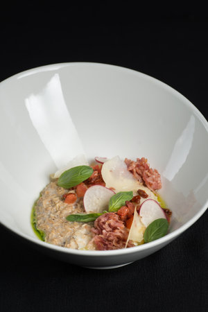 Bowl with delicious salted oatmeal, bacon and vegetables on a black tableclothの写真素材