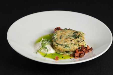 Zucchini pancakes served with sun-dried tomatoes and cream cheese on a black tableclothの写真素材