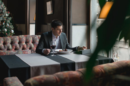 A young and attractive man uses his phone while eating veal tenderloin in ashes with grilled vegetables in an indoor restaurant. Business person work indoor conceptの写真素材