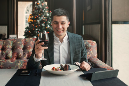 A young and attractive man uses his phone while eating veal tenderloin in ashes with grilled vegetables in an indoor restaurant. Business person work indoor conceptの写真素材
