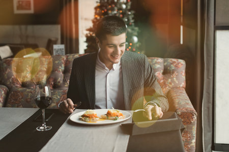 A young and attractive man uses his phone while eating veal tenderloin in ashes with grilled vegetables in an indoor restaurant. Business person work indoor conceptの写真素材