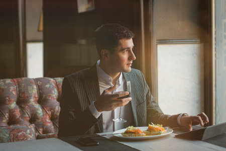 A young attractive man eating cottage cheese pancakes with sour cream and almond flakes and sea buckthorn-orange sauce in an indoor restaurant. Business person work indoor conceptの写真素材
