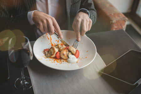 A young attractive man eating cottage cheese pancakes with sour cream and almond flakes and sea buckthorn-orange sauce in an indoor restaurant. Business person work indoor conceptの写真素材