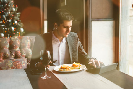 A young and attractive man uses his tablet while eating turkey fillet roll and pea puree in an indoor restaurant. Business person work indoor conceptの写真素材