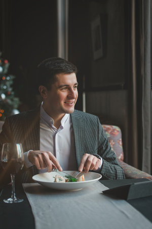 A young and attractive man uses his tablet while eating turkey fillet roll and pea puree in an indoor restaurant. Business person work indoor conceptの写真素材