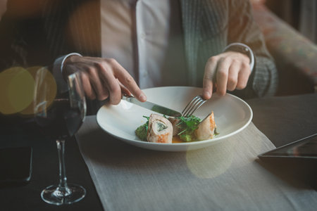 A young and attractive man uses his tablet while eating turkey fillet roll and pea puree in an indoor restaurant. Business person work indoor conceptの写真素材