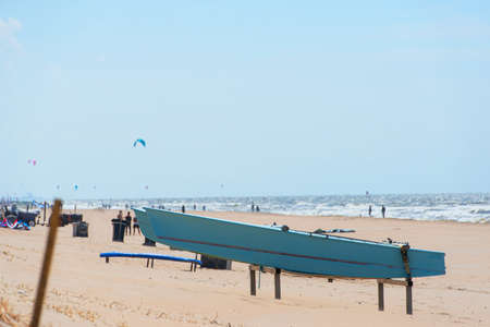Close up of a blue catamaran boat on a metal stand on the beach of Zandvoort in the Netherlands. kite of surfers viisible in the backgroundの写真素材