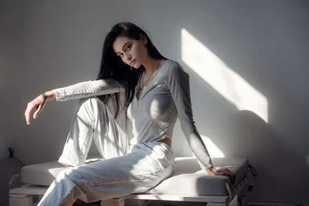 portrait of beautiful gentle woman in a white bodysuit posing in the sunshine. Black long hair. sensuality and tendernessの写真素材