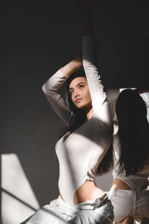 portrait of beautiful gentle woman in a white bodysuit posing in the sunshine. Black long hair. sensuality and tendernessの写真素材