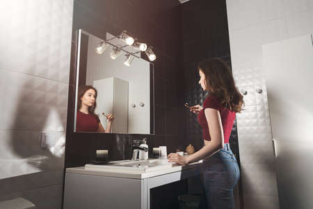 Woman brushing her teeth. Young woman in a burgundy top and jeanse with bamboo brush in front of the...