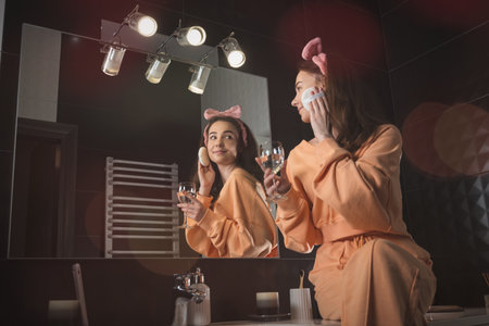 Pretty funny woman with mobile phone in the bathroom whit a glass of water in a hand. Skin careの写真素材