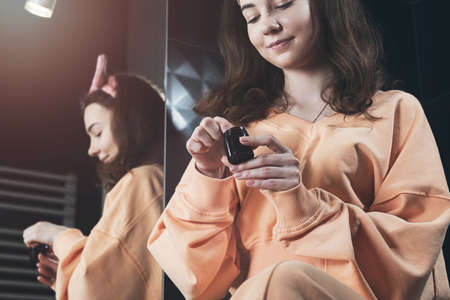 Woman is holding an open jar of cream and applies a small amount of the product to her hand. Concept...