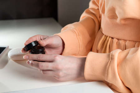 Woman is holding an open jar of cream and applies a small amount of the product to her hand. Concept of skin care, testing and selection of high-quality natural and organic cosmetics.の写真素材