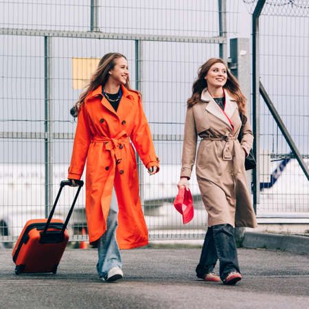 Two happy girls walking near airport, with luggage. Air travel, summer holidayの写真素材