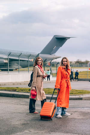 Two happy girls walking near airport, with luggage. Air travel, summer holidayの写真素材