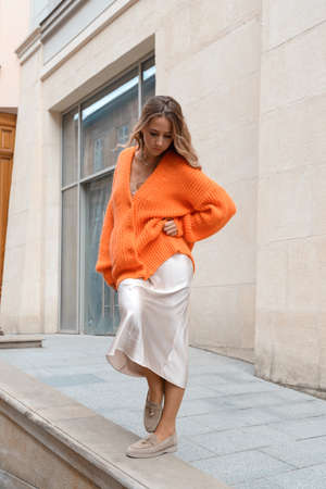 Portrait of fashionable women in orange sweater and beige dress posing in the streetの写真素材