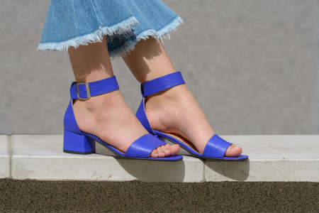 Womens legs in blue denim jeans and sandals in the city street. Trendy elegant casual outfit. Details of everyday summer look.の写真素材