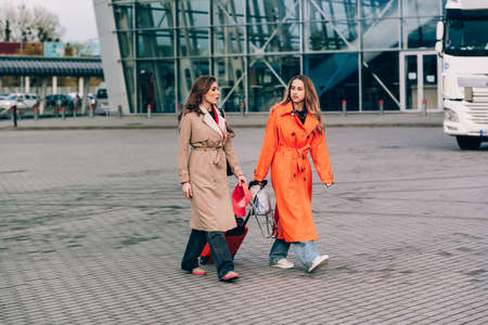 Two happy girls walking near airport, with luggage. Air travel, summer holiday