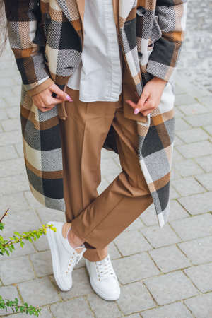 Closeup photo of beautiful fashionable woman wearing checkered long coat, beige pants, white blouse and sneakers.の写真素材