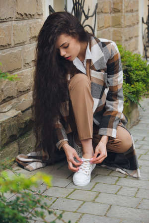 Closeup portrait of young beautiful fashionable woman wearing checkered long coat, beige pants and white blouse . Lady posing on city street.の写真素材