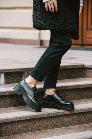 Close-up photo of young woman in black fur coat, jeanse and shoes posing on stairsの写真素材