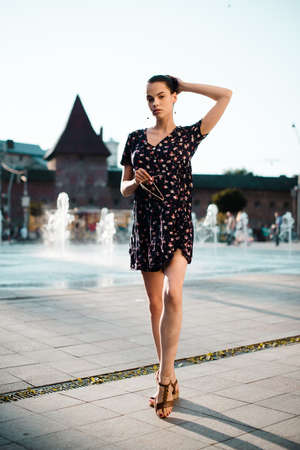 Portrait of a stylish young woman. Brunette with ballerina hairstyle in sundress posing on street....
