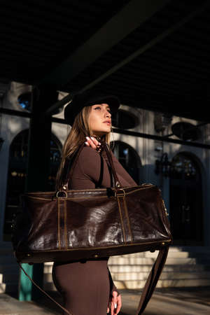 Fashionable young brunette woman wearing Solid Long Sleeve Bodycon One Piece Jumpsuits posing with a leather brown travel bagの写真素材