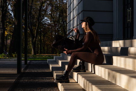 Fashionable young brunette woman with long legs wearing Solid Long Sleeve Bodycon One Piece Jumpsuits posing with a leather brown travel bagの写真素材