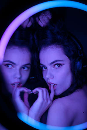 Emotional studio portrait of a young woman in a wireless headphones with ring flash effect. Round LED Circle Lamp.の写真素材