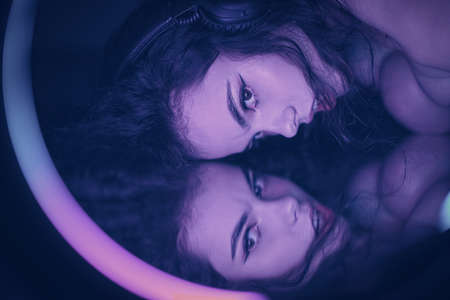 Emotional studio portrait of a young woman in a wireless headphones with ring flash effect. Round...